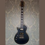 Černá elektrická kytara typu singlecut s hnědým lemováním. Na hlavě je zlaté logo Ltd a nápis ESP. Kytara má dva humbuckery se zlatými kryty, zlatý m…