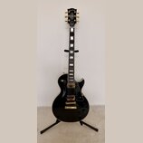 Černá elektrická kytara s gold hardwarem umístěná na černém stojanu. Na hlavě hmatníku je bílý nápis Epiphone. Kytara má dva humbuckery, zlatý most a…