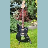 Černá elektrická kytara s tmavým hnedým hmatníkem a světlou hlavou. Na těle je černý pickguard, dva snímače s bílými plastovými krytkami a chromovaný…