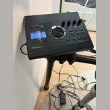 Černý elektronický bicí modul s displejem, na kterém je nápis "KIT 100 User Kit". Na spodní hraně je logo "Roland" a vpravo nápis "DRUM SOUND MODULE…