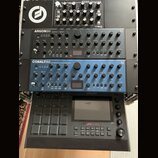Fotografie zobrazuje čtyři hudební zařízení v racku. Shora dolů jsou vidět moduly Moog MINITAUR, Argon8M a Cobalt8M v modré barvě, a ve spodní části…