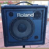Černý kombozesilovač s povrchem z textilie a kovovou ochrannou mřížkou. Na mřížce je nápis Roland a v dolní části logo KC s doplňkem KEYBOARD AMPLIFI…