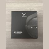 Černá čtvercová krabice s obrázkem sluchátek. Na horní části je bílé logo a nápis beyerdynamic, vpravo je uveden model DT 770. V levém dolním rohu je…