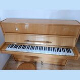 Světle hnědé pianino s lakovaným dřevěným povrchem. Na krytu nad klávesnicí je viditelný nápis "SMILE". Nástroj vykazuje známky opotřebení v podobě š…