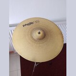 Zlatý kovový činel umístěný na stojanu. Na povrchu je černý nápis PAiSte 302 a pod ním menší text 20" Ride. Povrch činelu vykazuje drobné škrábance a…