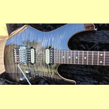 Elektrická kytara s tmavým lakovaným povrchem a viditnou strukturou dřeva. Nástroj má dva humbuckery, chromovaný most s páčkou a dvě ovládací knoflík…