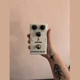 Bílý kytarový efekt s nápisy NUX, ad-3 a ANALOG DELAY. Na horní straně jsou tři černé otočné ovnovky s popisky TIME, REPEAT a MIX. V dolní části je k…