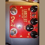 Červený kytarový efekt s nápisy LANCELOT DISTORTION a D.T. na horní straně jsou čtyři černé otočné knoflíky s popisky MORE, TONE, OUTPUT a GAIN. Na p…