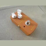 Oranžový kytarový efekt s bílými oválovými knoflíky. Na horní straně jsou nápisy Volume, Focus, Sweet Baby, Overdrive, OUT, 9V DC a TRUE BYPASS, v pr…