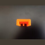 Na fotografii je malý, oranžový plastový dílek obdélníkového tvaru s výřezem v dolní části. Povrch je hladký a bez viditelných nápisů či log. Dílek v…
