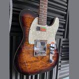 Elektrická kytara typu Telecaster s hnědým slunečním odstínem (sunburst) a výraznou plamenovitou strukturou dřeva. Nástroj má perleťový pickguard a h…