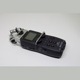 Černý digitální záznamový přístroj s LCD displejem a stříbrným kovovým rámem kolem mikrofonů. Na přístroji jsou bílé nápisy ZOOM, H5 Handy Recorder,…