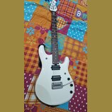 Bílá elektrická kytara s tmavým hnedým hmatníkem. Na hlavě je viditelné logo MUSIC MAN. Kytara má dva humbuckery, tremolo s páčkou a tři ovládací kno…
