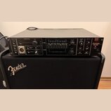 Černý rackový přístroj s nápisem Roland VOCODER SVC-350 položený na černém kombu značky Fender. Přední panel obsahuje různé přepínače, potenciometry…