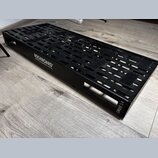 Černý kovový pedalboard s perforovaným povrchem a bočními úchopy. Na boku je bílý nápis ROCKBOARD by WARWICK a v pravém dolním rohu označení CINQUE 5…