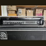 Černý basový zesilovač v kovovém šasi s nápisem Ampeg SVT-3 PRO. Přední panel obsahuje ovládací knofíky s popisky INPUT, GAIN, BASS, MIDRANGE, FREQUE…