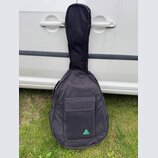 Černý textilní pouzdro (gig bag) na kytaru s přední kapsou. V dolní části kapsy je viditelné tyrkysové trojúhelníkové logo s nečitelným nápisem uvnit…