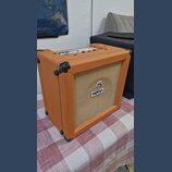 Kytarový kombozesilovač v oranžovém vinylu s béžovou textilní maskou. Na přední straně je bílý obdélníkový štítek s nápisem ORANGE a nad ním malý bar…