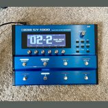 Modrý kytarový syntetizátor s nápisem BOSS SY-1000 GUITAR SYNTHESIZER. Zařízení má digitální displej, na kterém je zobrazen text 02-2 a WARM DREAD NO…