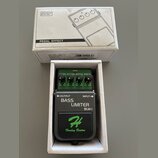 Efektový pedál v bílém kartonovém boxu s nápisem PEDAL EFFECT a nákresem komba. Pedál je zelený a černý s nápisy OUTPUT, INPUT, BASS LIMITER a BLM-I.…