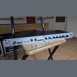 Rackové zařízení s bílým předním panelem a černým šasi. Na levé straně je logo dbx PROFESSIONAL PRODUCTS, vpravo nápis 286s Mic Preamp Processor. Pan…