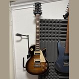 Elektrická kytara s tónem sunburst v hnědých odstínech a krčkem z tmavého dřeva. Na hlavě je bílý nápis Gibson a pod ním stylizovaný nápis Les Paul.…