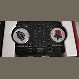 Černý DJ 컨트롤러 Pioneer Dj s logem serato v dolní části. Zařízení má dva stříbrné jog-wheels, z nichž oba jsou zakryty nálepkami; na levém je nápis The…