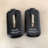 Dvě černé bezdrátové vysílače/přijímače s kovovými konektory. Na obou je bílý nápis „Harley Benton“ a pod ním text „AIRBORNE WI-2.4GHZ INSTRUMENT“. P…