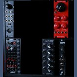 Fotografie zachycuje několik modulů syntezátora v černém racku. V horní části je vlevo šedý modul s nápisy GLIDE, CLK, MOD a BLACK MIDI-CV od erica s…