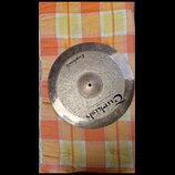 Kruhový činel z kovu s viditelnou vykovanou strukturou povrchu. Na povrchu je nápis „Euphonic“ a logo „Turkish“ s doplňujícím textem „handmade cymbal…