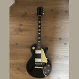 Černá elektrická kytara s tvarem typu Les Paul a krémovým pickguardem. Na hlavě hmatníku je bílý nápis Era. Nástroj má dva humbuckery s krémovými rám…