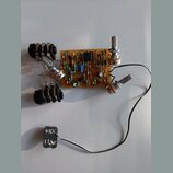 Fotografie zobrazuje ručně sestavený elektronický obvod na hnědé perforované desce s různými součástkami. Na desce jsou připájena tři potenciometry,…