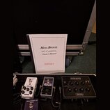 Na fotografii je otevřený transportní kufr s několika efektovými pedály a uživatelskou příručkou. Na bílém sešitě je nápis MESA/BOOGIE, M3 CARBINE. O…