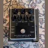 Černý basový předzesilovač v kovovém šasi s nápisy MICROTUBES B7K, ANALOG BASS PREAMP a DARKGLASS ELECTRONICS - MADE IN FINLAND. Zařízení má sedm čer…