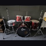 Vícedílná bicí souprava v tmavě červené barvě s chromovaným kováním. Na basovém bubnu je bílé logo Gretsch, stejné logo je viditelné i na ostatních b…