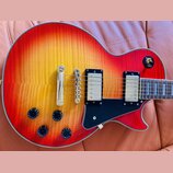 Elektrická kytara s trupem v červeno-žlutém sunburst provedení a viditnou strukturou dřeva. Nástroj má dva humbuckery s kovovými kryty, černý pickgua…