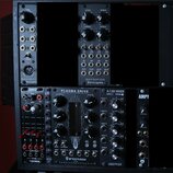Fotografie zachycuje modulární syntetizátor v racku. V horní části jsou moduly s nápisy BLACK MIDI-CV erica synths a BLACK QUAD VCA2 erica synths. Sp…