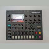 Černý polyfonní digitální syntetizátor s nápisem Elektron v pravém horním rohu. Zařízení obsahuje displej s textem Polyphonic Digital Synthesizer a D…