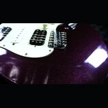 Detail elektrické kytary s tmavě fialovým metalizovaným povrchem s třpytivým efektem. Nástroj má bílý pickguard, tři snímače (dva jednoduché a jeden…