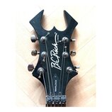 Černá hlava elektrické kytary s výrazným, ostře zakončeným tvarem. Na povrchu je bílý nápis B.C. Rich, N.J. Series a v dolní části označení WARLOCK.…