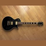 Černá elektrická kytara s tvarem singlecut a bílým lemováním. Na hlavě je viditelné logo Epiphone. Nástroj má dva humbuckery, zlatý hardware a hриф s…