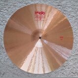 Kruhové činely z bronzu s viditelným broušením povrchu. Na horní části je červené logo Paiste 2002 s nápisy TRADE MARK a MADE IN SWITZERLAND. V pravé…