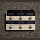 Stříbrný MIDI kontrolér s nápisy SINGULAR SOUND a MIDI MAESTRO. Zařízení má dvě řady tří modrých displejů a dvě řady tří kulatých kovových tlačítek.…