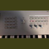Detailní záběr na ovládací panel stříbrného syntezátoru s klávesami. Panel obsahuje několik sad tlačítek, otočný knoflík SPEED a sekci ARPEGGIATOR s…