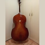 Fotografie zachycuje zadní stranu smyčcového nástroje, pravděpodobně violoncella, v hnědém lakovaném provedení. Nástroj je vyroben ze dřeva a vykazuj…
