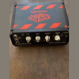 Černý basový zesilovač s červenými šikmými pruhy na horní straně. Na vrchu je nápis Quilter BASS BLOCK 800 a na předním panelu vpravo text BASS BLOCK…