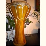 Dřevěný buben typu djembe s hnědým povrchem a viditelnou strukturou dřeva. Horní obruč je potažena světlým materiálem s ozdobným vzorem a k tělu je p…