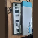 Stříbrný MIDI kontrolér s klávesami a černým rámem. Na pravé straně je nápis swissonic Easykey 49. Vedle nástroje leží černý USB kabel a bílo-modrá k…