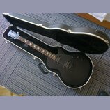 Černá elektrická kytara s tvarem singlecut v otevřeném černém tvrdém kufru. Na hlavě je viditelné logo ESP. Kytara má dva humbuckery, dvě kontrolní k…