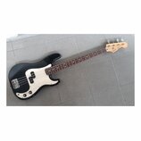 Černá elektrická basová kytara s bílým pickguardem a hnědým hmatníkem. Na hlavě nástroje je viditelné logo Squier a nápis Precision Bass. Povrch kyta…